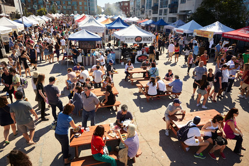 A panoramic scene of people & tents at an outdoor summer festival.